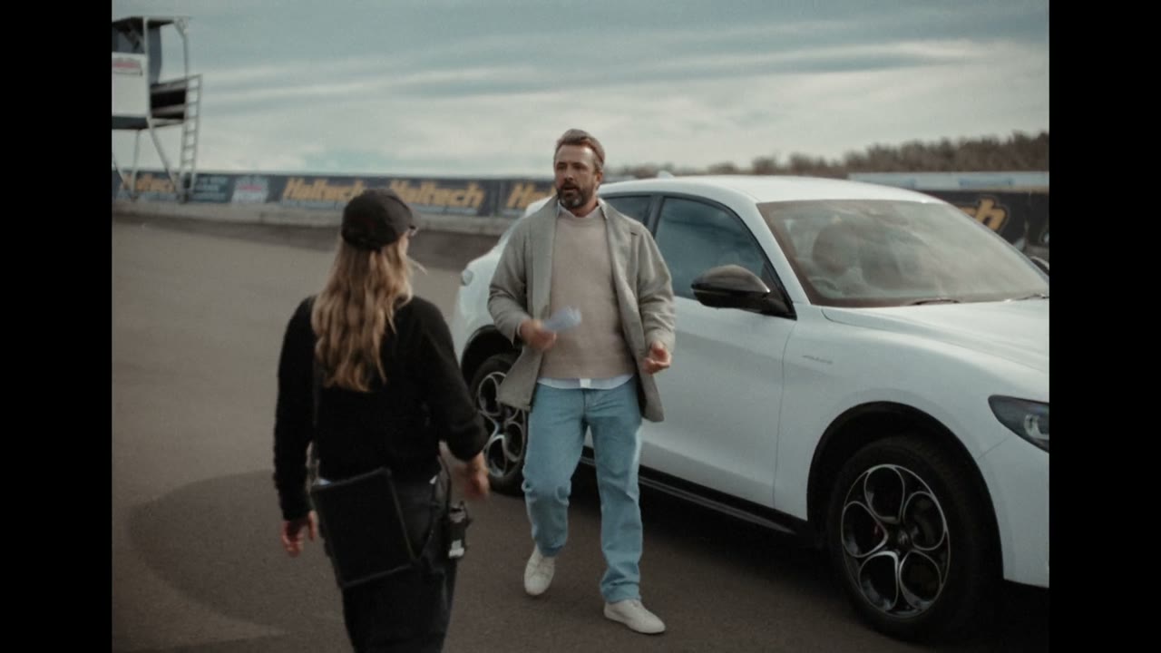 Still from Alfa Romeo 'Four-Leaf Clover': two people beside a white Alfa Romeo SUV on an overcast racetrack